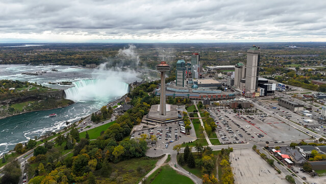 Majestic aerial view of Niagara Falls with the iconic Skylon Tower standing tall amidst a vibrant cityscape, surrounded by lush greenery and a dramatic cloudy sky, Ontario, Canada