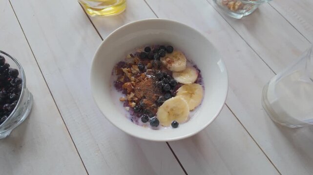 Cinnamon sprinkled over oatmeal with berries and banana, slow motion healthy breakfast finishing touch