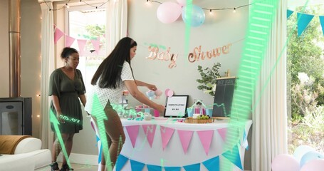 Fototapeta premium Placing baby shower table at home women wearing white top and green dress arranging bunting cakes