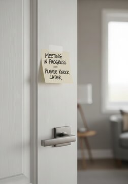 Handwritten note reading &ldquo;Meeting in Progress &ndash; Please Knock Later&rdquo; taped to a minimalist home office door, representing professional boundary communication in remote work culture