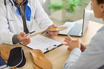 Orthopedist doctor shows orthopedic insoles to patient in medical clinic. They discuss custom...