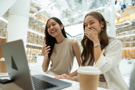 Asian women laughing watching laptop screen together