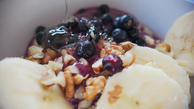 Macro slow motion honey drizzle over blueberries, walnuts and banana on oatmeal, natural sweet healthy breakfast topping
