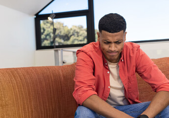 Man in coral shirt leaning forward on sofa in living room by black-framed windows, copy space