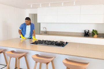 Obraz premium Man cleaning kitchen island with gas cooktop using cloth and yellow rubber gloves, copy space