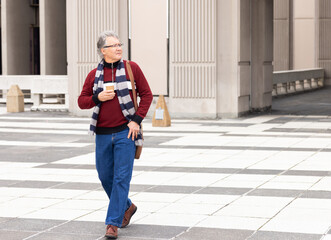 Senior man walking across tiled plaza by grooved columns, wearing striped scarf, carrying coffee © wavebreak3