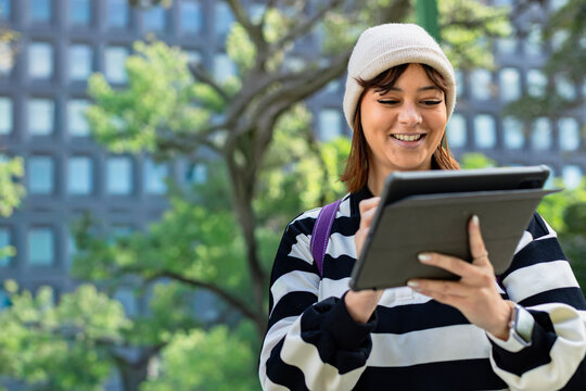 Mid-adult woman in beanie tapping tablet in folio at park with stylus purple strap, copy space