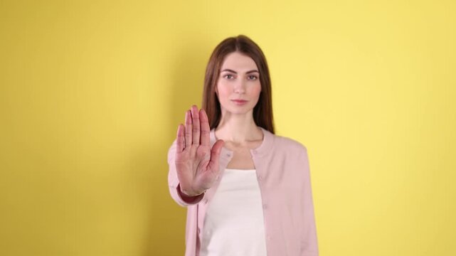 Woman making stop gesture on yellow background