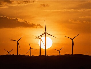 Fototapeta premium Wind turbines are silhouetted against a massive bright sun during a dramatic sunset over a hilly landscape showing sustainable energy production power
