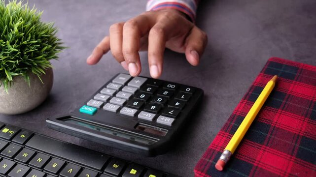 A close-up view of male hand calculating using a calculator and taking notes on a diary while working from home office