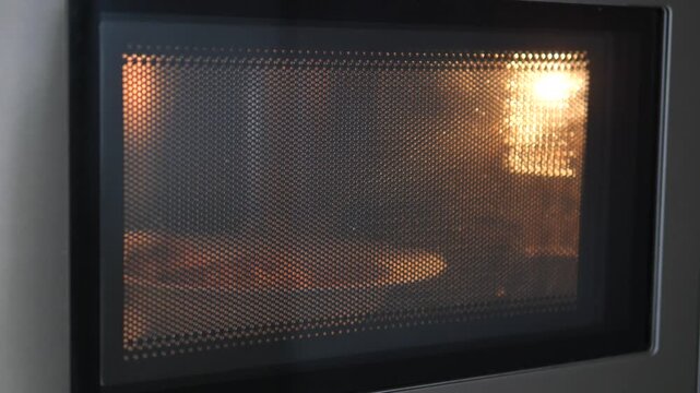 Plate of food spinning inside working microwave oven with glowing internal light