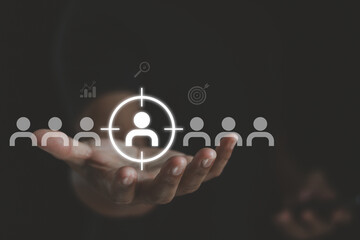 Obraz premium Businessman hand holding virtual target icon over group of people. Customer targeting, audience segmentation, recruitment strategy and data driven marketing concept for business growth.