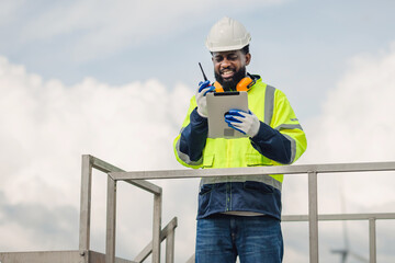 man in a yellow and black safety vest is standing on a railing with a tablet in his hand