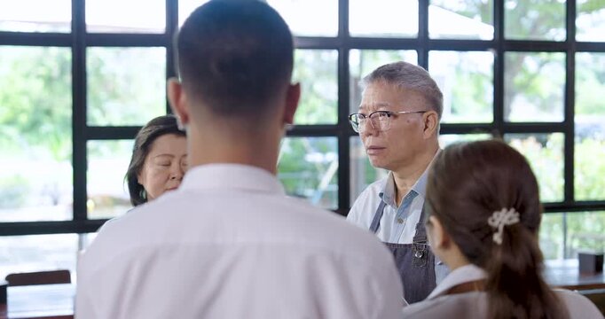 Senior asian cafe owner gives final instructions to young employees, teamwork cooperation enhances service readiness, leadership and communication strengthen coordination in small restaurant business