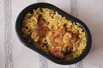 Chicken with rice in a black container on a light tablecloth