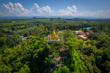 Fototapeta premium Aerial drone view of golden pagoda at Wat Prangkasi in Thong Pha Phum, Kanchanaburi, Thailand surrounded by lush forest mountain landscape