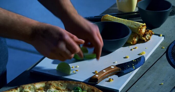 Closeup of cook cutting lime and squeezing it above veggie pizza