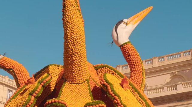 Heron citrus sculpture at Fete du Citron in Menton France with historic architecture in background. Lemon Festival artistic installation.