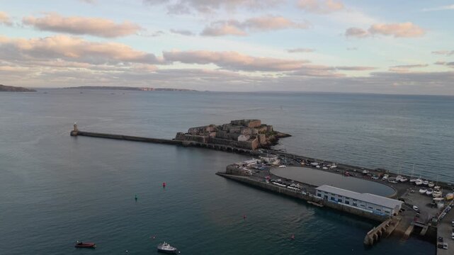 359
High reveal drone footage of St Peter Port harbour Guernsey Channel Islands from Castle Cornet revealing entrance and outer harbour in late afternoon sunlight