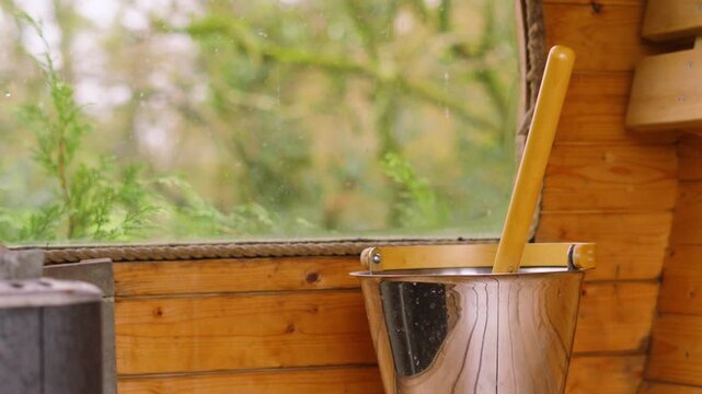Slow pan from wood fire in sauna to ladel with water ready to create steam for heating up room. Luxury spa treatments, self-care routines, stress reduction. Part of routine for health and longevity.