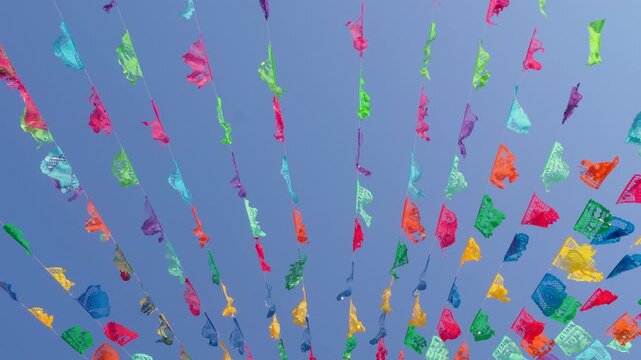 Festive garlands of colorful cut-out paper hung as decoration waving against a blue sky. Papel picado.