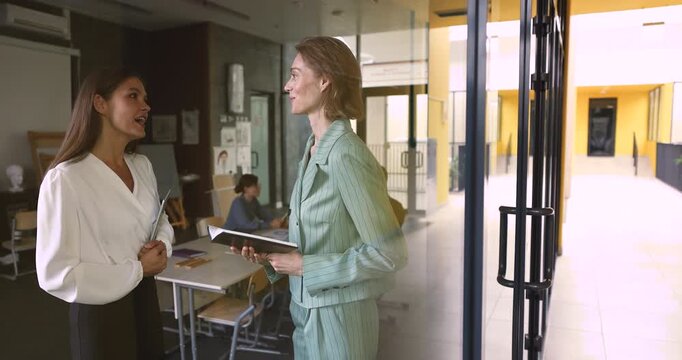 Two older adult businesswomen, colleagues or coworkers standing in modern coworking office discussing joint task or project details, handshaking, finalizing meeting. Assistance, business partnership