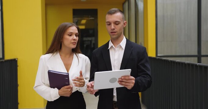 Team members leading work-related conversation while walking along office hallway, discussing project, share opinion or thought, handshaking as business gesture of respect, successful teamwork result