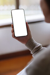 Vertical mockup image of a woman holding and using mobile phone with blank desktop screen at home