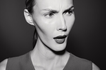 Fototapeta premium White woman with pale skin shows confused expression in black and white close-up portrait with dark background. Concept for emotion and doubt.
