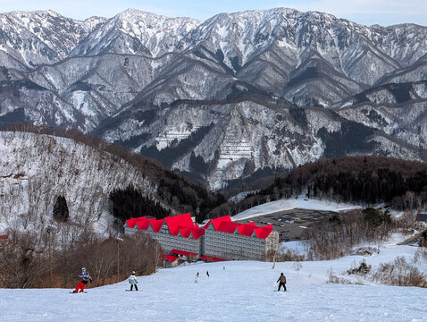 People skiing down a snowy mountain slope towards a large hotel with red roof