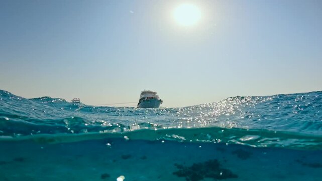 Half underwater view of rough sea waves and anchored yachts in the horizon