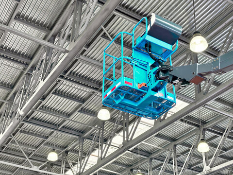 Construction crew using aerial lift to inspect high ceilings in a large warehouse during daytime work hours