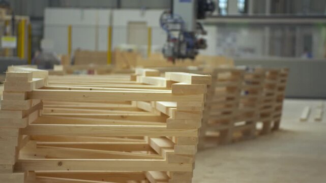 Stack of unfinished wooden pallets in a manufacturing facility with machinery in the background