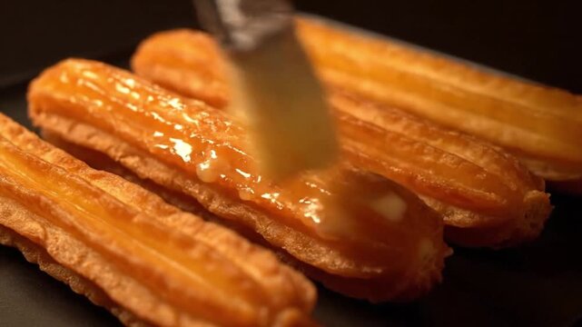 Pastry brush glazing crispy golden fried churros with sweet syrup