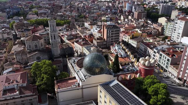 A sweeping aerial pan across Figueres, showcasing the Sant Pere church tower and the glass geodesic dome of the Dali Theatre-Museum under a clear sky