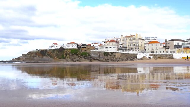 Low angle view of Praia das Ma&ccedil;&atilde;s with reflective wet sand and white cliffside houses above the Atlantic coast.