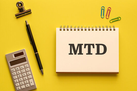Eye-catching image of MTD text on notebook. The word stands for month to date. Shown with calculator, pen, clips.