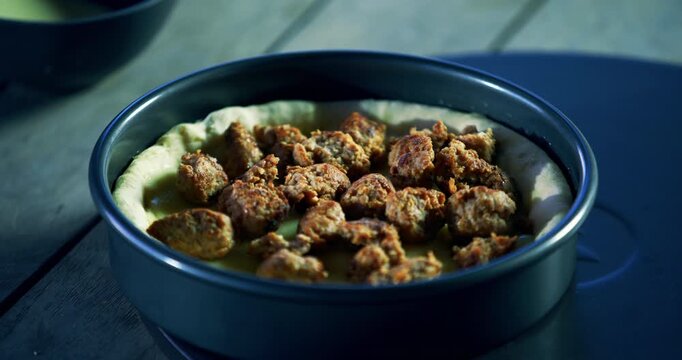 Cook's hands placing cut up meat in tray of pizza dough - closeup shot