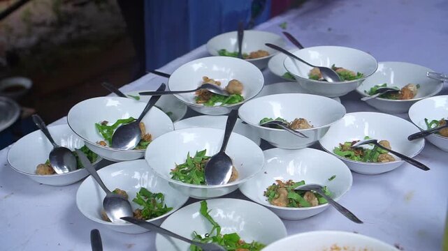 Multiple white bowls of Indonesian meatball soup with greens and spoons set on table for catering service, representing event dining, culinary buffet, and local food.