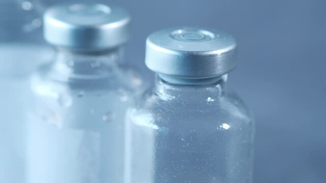 Medical vaccine glass vials with silver caps under soft studio lighting on blue background