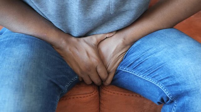 Man sitting on sofa suffering from pain in crotch area and groin