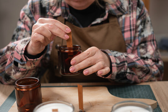 Candle maker putting wooden wick into glass jar in workshop. making aroma candles.