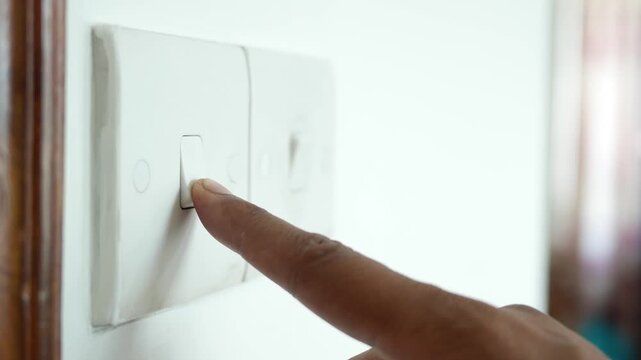 Close up of finger pressing light switch for electricity power on white wall