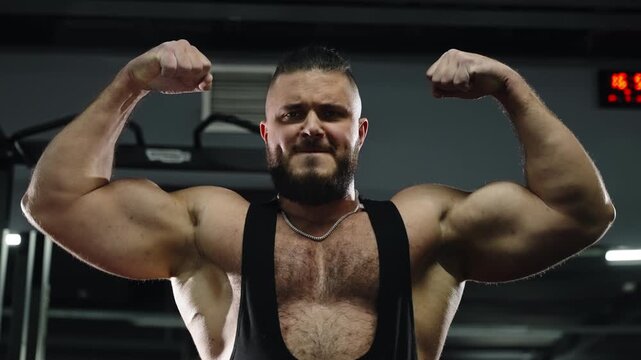 Close-up of a muscular bearded athlete doing an intense shoulder workout with arms extended in a lit gym, highlighting strength, focus, and definition in the chest and deltoids.