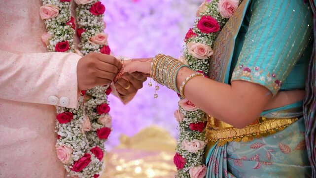 Indian bride and groom exchanging rings during a traditional wedding ceremony. Close-up of hands with floral garlands and elegant cultural attire during engagement ritual.