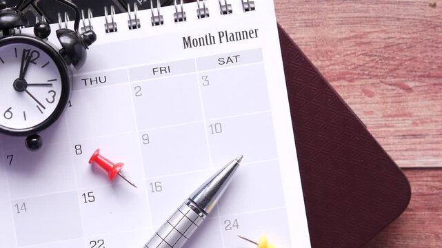 Close up of month planner with alarm clock and pen on wooden table, planning concept footage