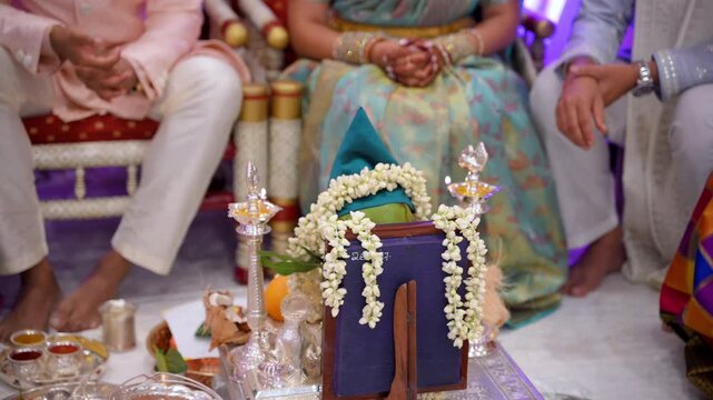 Indian or Pakistan couple seated in traditional attire during a wedding ceremony ritual. Close up view of hands performing cultural wedding customs with decorative elements and ceremonial setup.