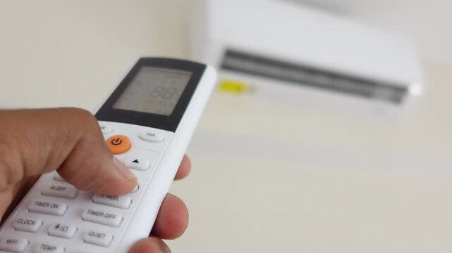 Close up of person hand operating remote control to adjust settings on modern air conditioner unit for comfortable room temperature