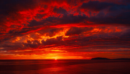 Fiery red sunset over ocean with dramatic clouds reflecting intense orange and red light, golden hour seascape with silhouette of land on horizon, vibrant and powerful sky display at dusk