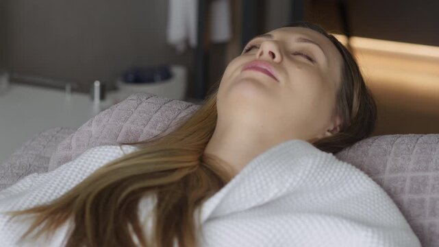 Young woman lying on spa treatment couch with automatic backrest lifting, wellness and relaxation procedure in modern beauty center.